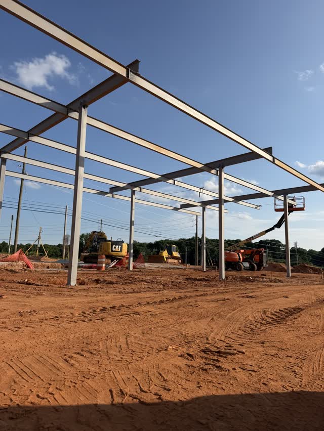 A run of steel canopy columns and beams part way through erection on a dirt pad