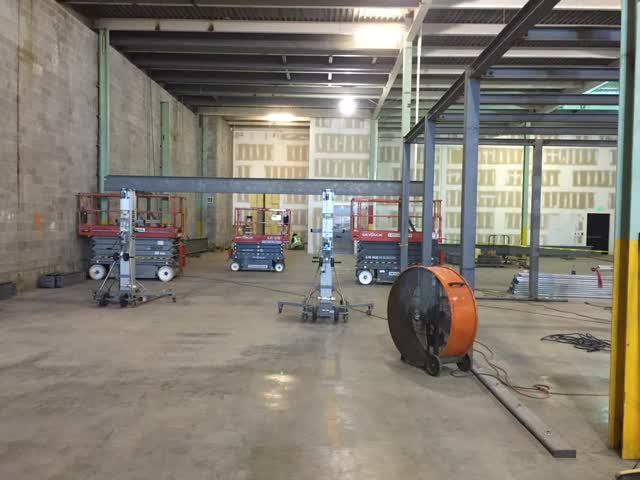 Steel beams and columns erected inside an existing masonry building shell with scissor lifts on the slab