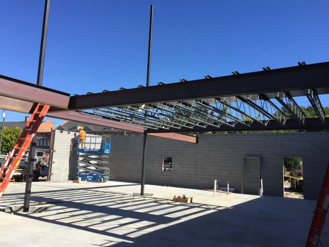Crew setting open-web steel joists from lifts inside a building shell