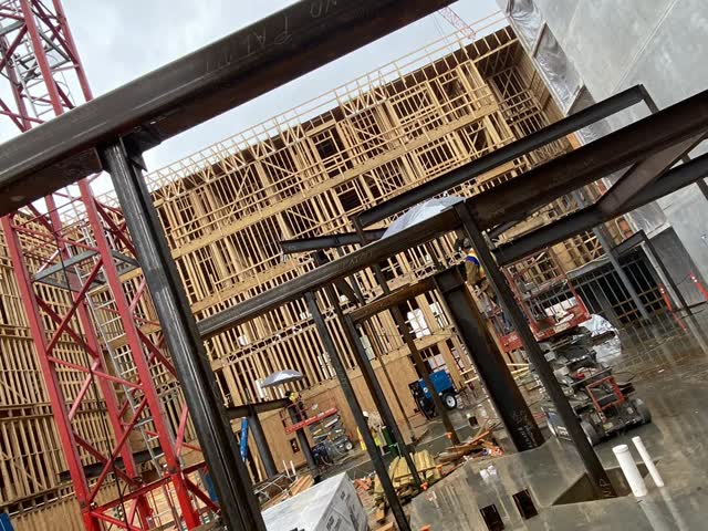 Steel framing going up between a concrete podium and wood framing on a multi-family site